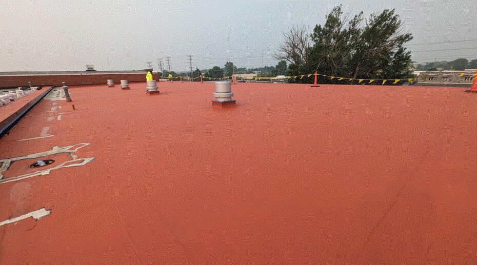 A flat red roof with several vents and pipes, some areas with visible wear and patches. Safety caution tape is strung along the edge, and trees, power lines, and buildings are visible in the background.