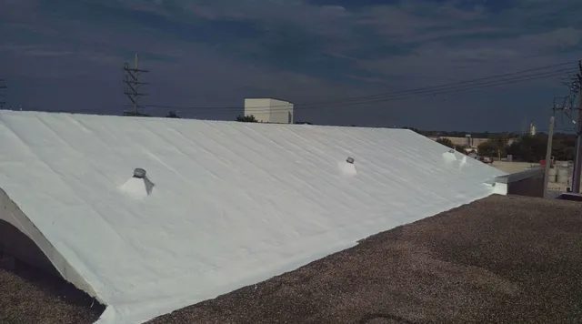 A white-painted sloped roof with three vent pipes, pictured under a partly cloudy sky, with power lines and several buildings visible in the background.