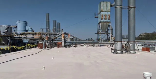 A flat industrial rooftop with several large ventilation pipes, ducts, and machinery under a clear blue sky. Yellow caution tape is visible on the left side of the roof.
